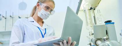 Mulher loira vestindo branco em um laboratorio, segurando um notebook, representando o software para laboratorio clinico